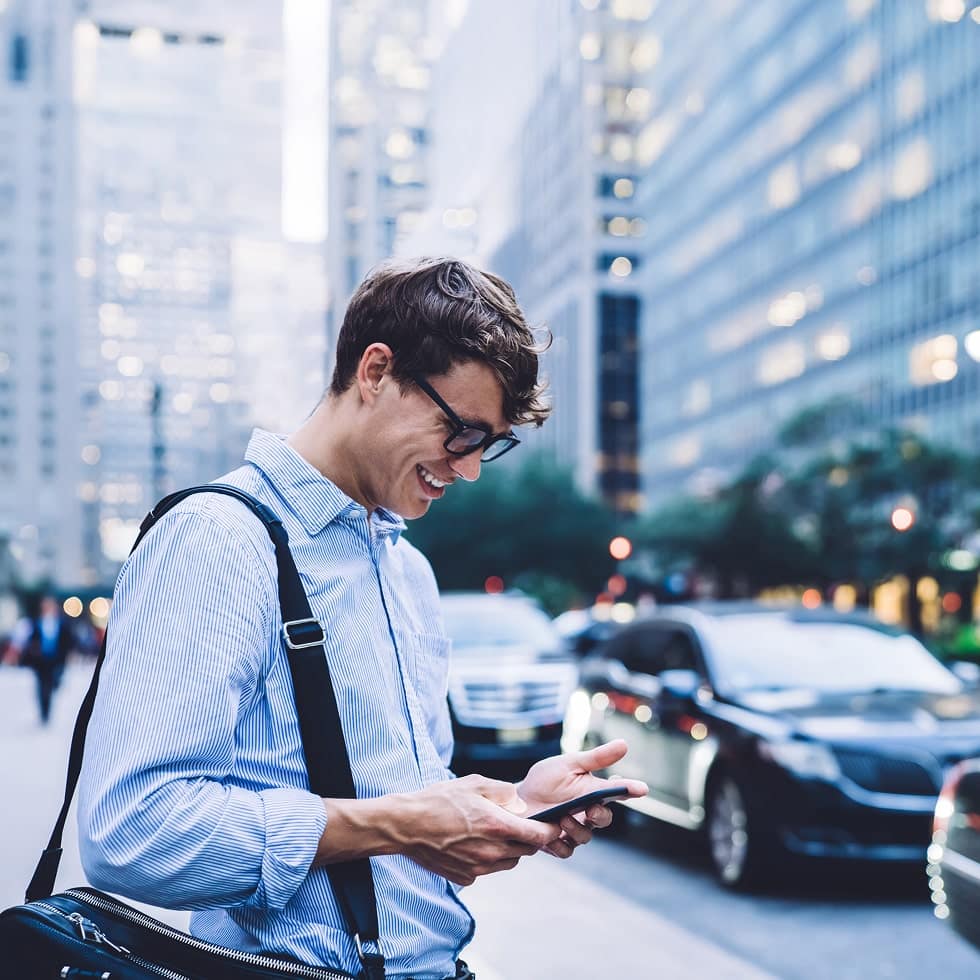 person on city sidewalk smiling while using smartphone